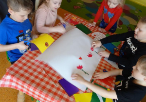 Piątka dzieci przygotowuje plakat, naklejają tulipany z papieru.